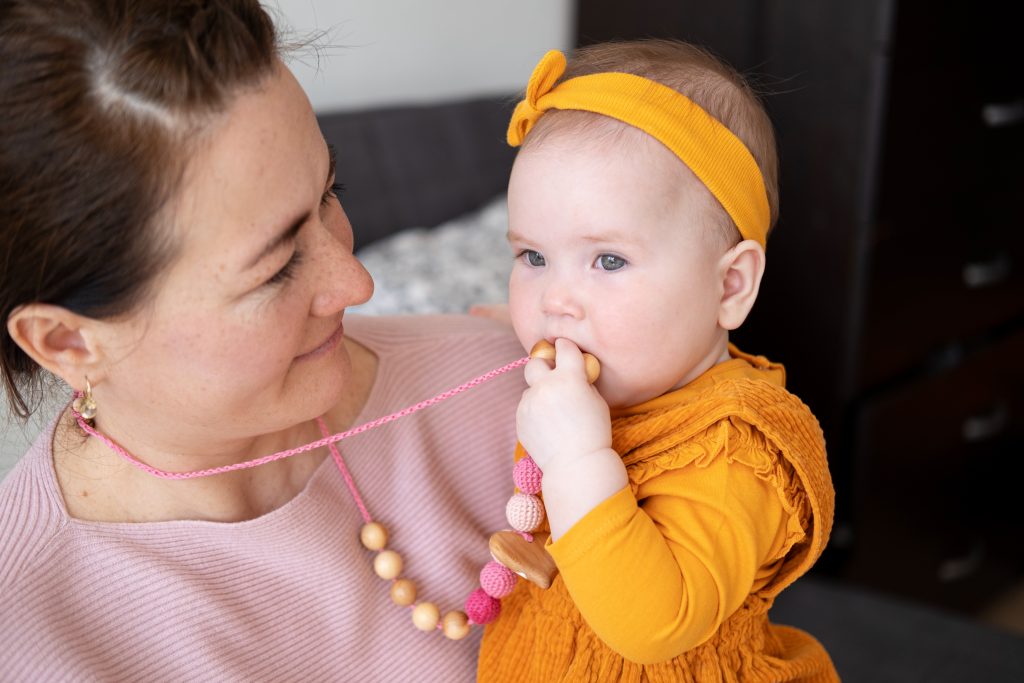 woman carrying her baby daughter baby girl touching teething beads